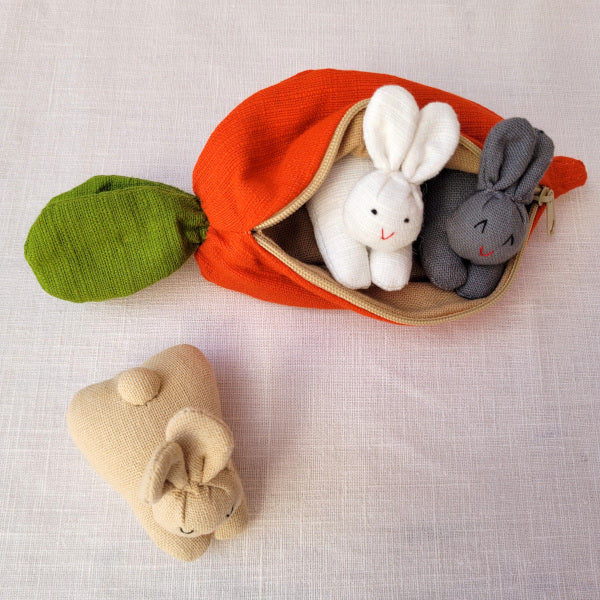 A carrot purse bursting with three multicultural bunnies
