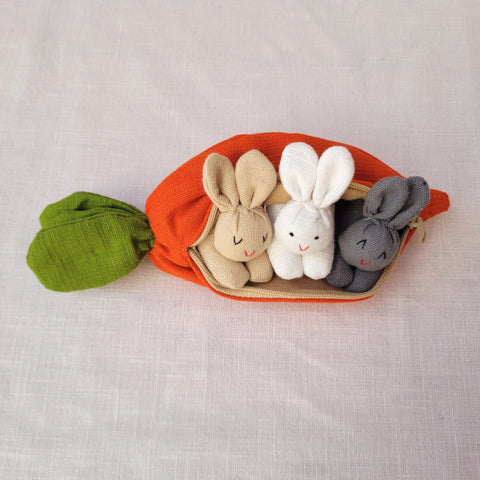 A carrot purse bursting with three multicultural bunnies